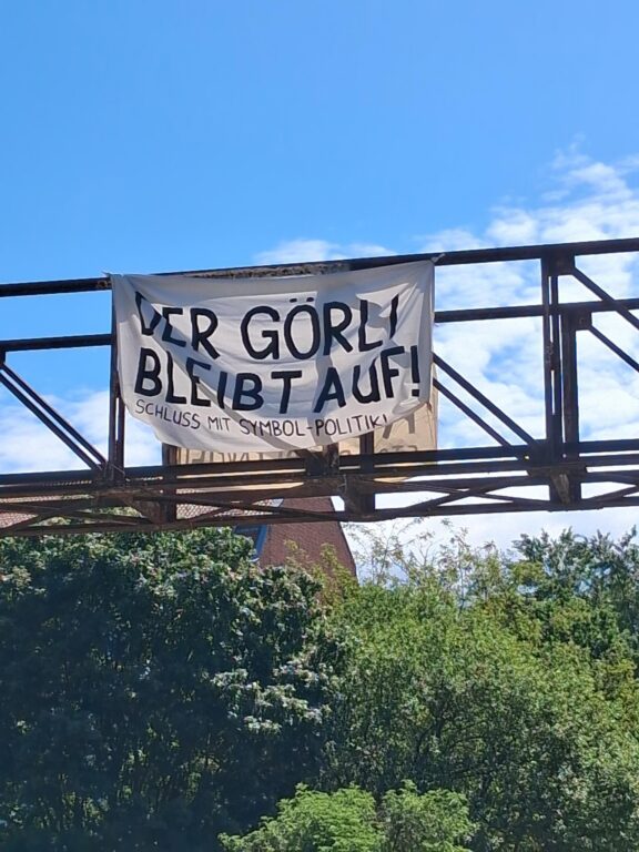 Transparent 'Der Görli bleibt auf! Schluss mit Symbol-Politik!' hängt an einer Brücke über Bäumen