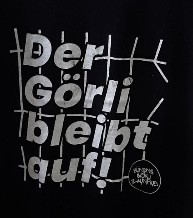 Siebdruck-Schriftzug „Der Görli bleibt auf!“ in Zaunoptik auf schwarzem Stoff, mit Logo Bündnis Görli Zaunfrei.