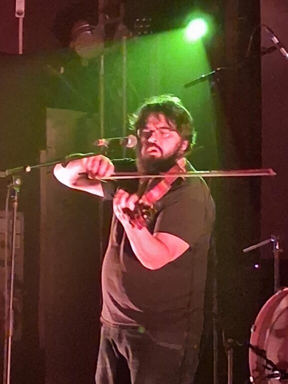 Musiker spielt konzentriert Geige auf einer Bühne im grünen Bühnenlicht.