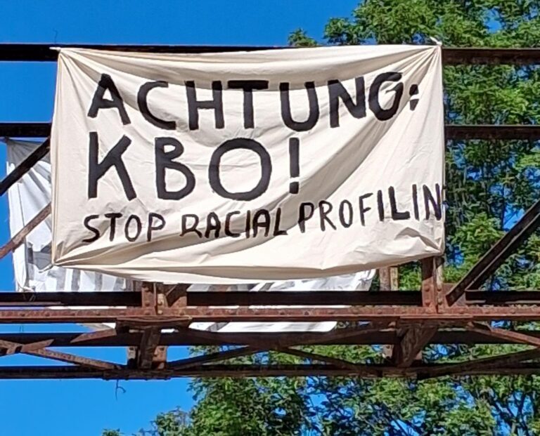 Transparent an einem Metallgerüst mit der Aufschrift „Achtung: KBO! Stop racial profiling“