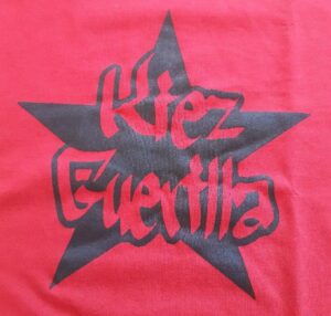 Rotes T-Shirt mit schwarzem Sternlogo und Schriftzug 'Kiez Guerilla'