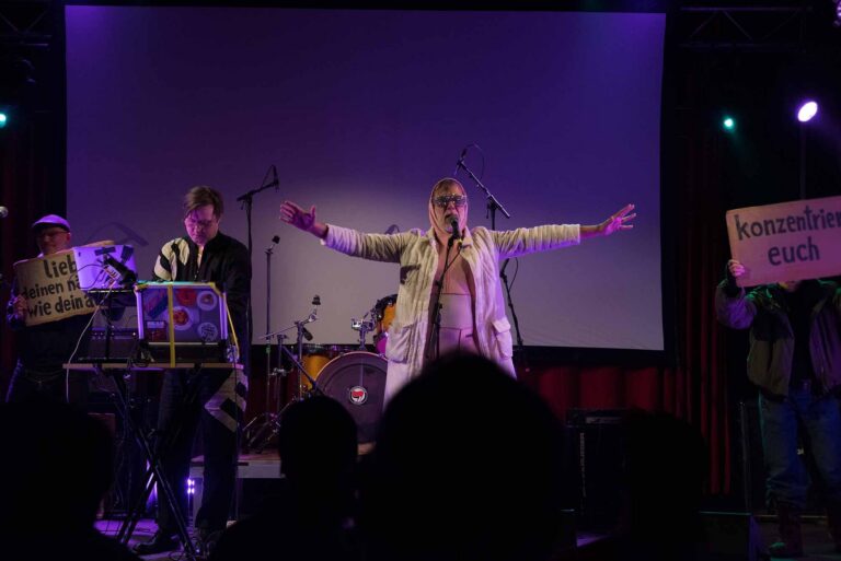 Auftritt auf einer Bühne mit Nebel und Lichtshow, im Publikum ein Schild 'konzentrier euch'