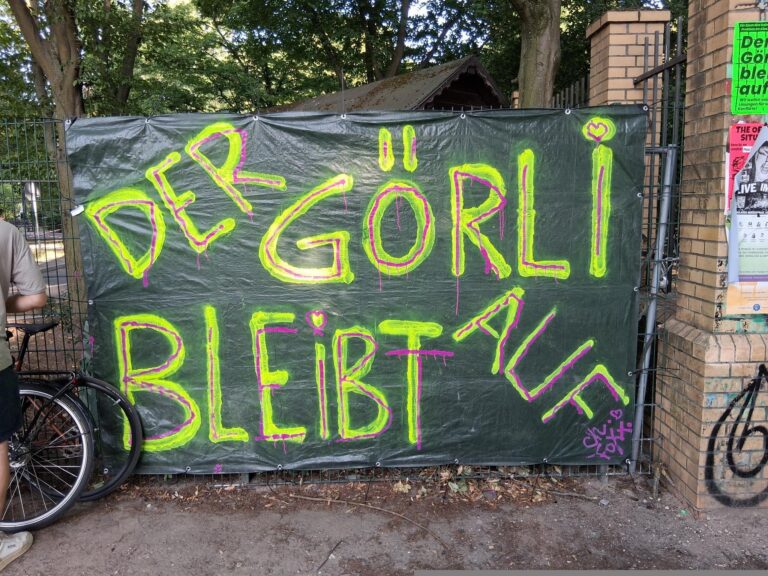 Grüne Plane an einem Zaun, besprüht mit „Der Görli bleibt auf“, davor ein abgestelltes Fahrrad