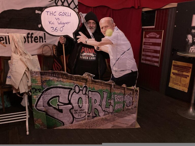 Foto bei einer Veranstaltung: zwei Personen posieren an einer Pappfigur-Kulisse mit Graffiti „Görli“ und Schild „THC Görli vs. Kai Wegner 36:0“.
