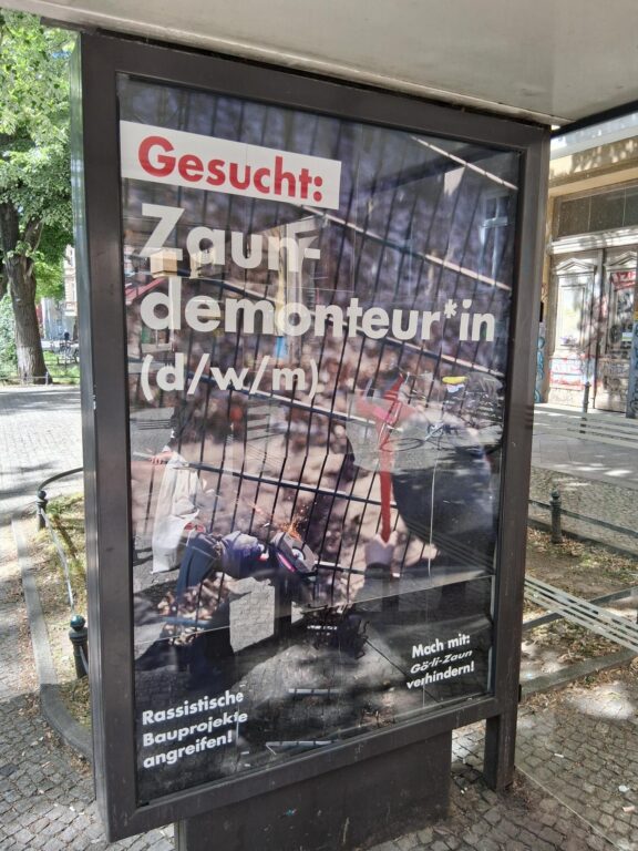 Werbeplakat an einer Bushaltestelle: 'Gesucht: Zaundemonteur*in (d/w/m) – Rassistische Bauprojekte angreifen!'